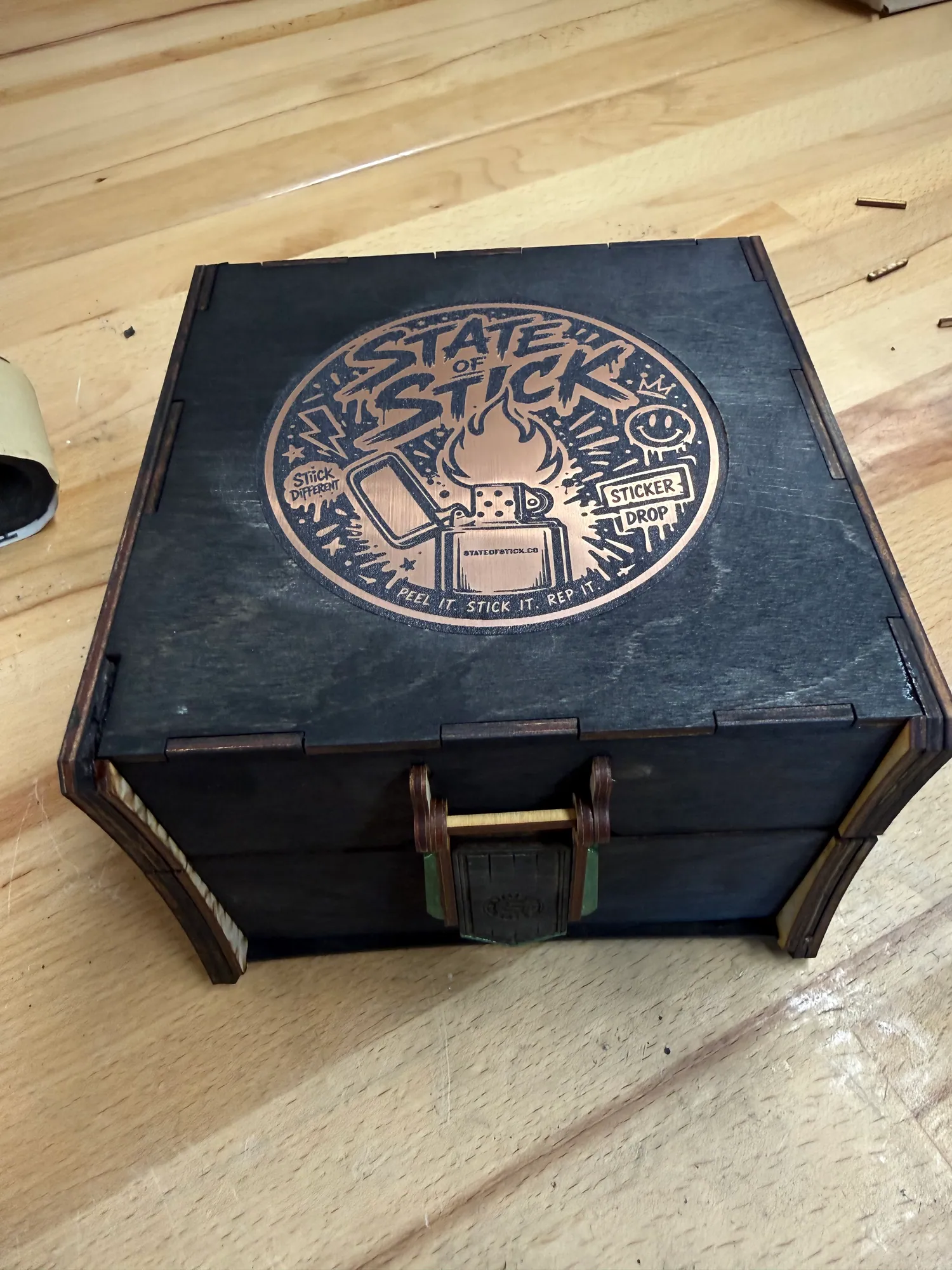 Closed black laser-cut display box with a copper State of Stick, Co. emblem and custom latch